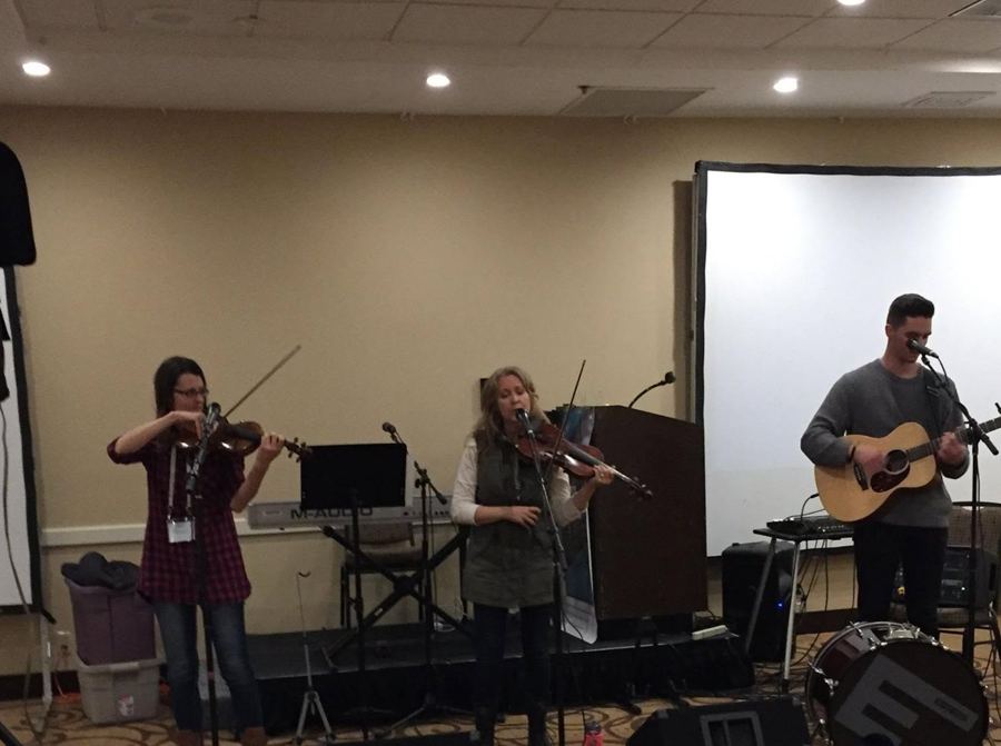 Kate White and fellow musicians performing with violins and guitar at an Ivory Garden conference